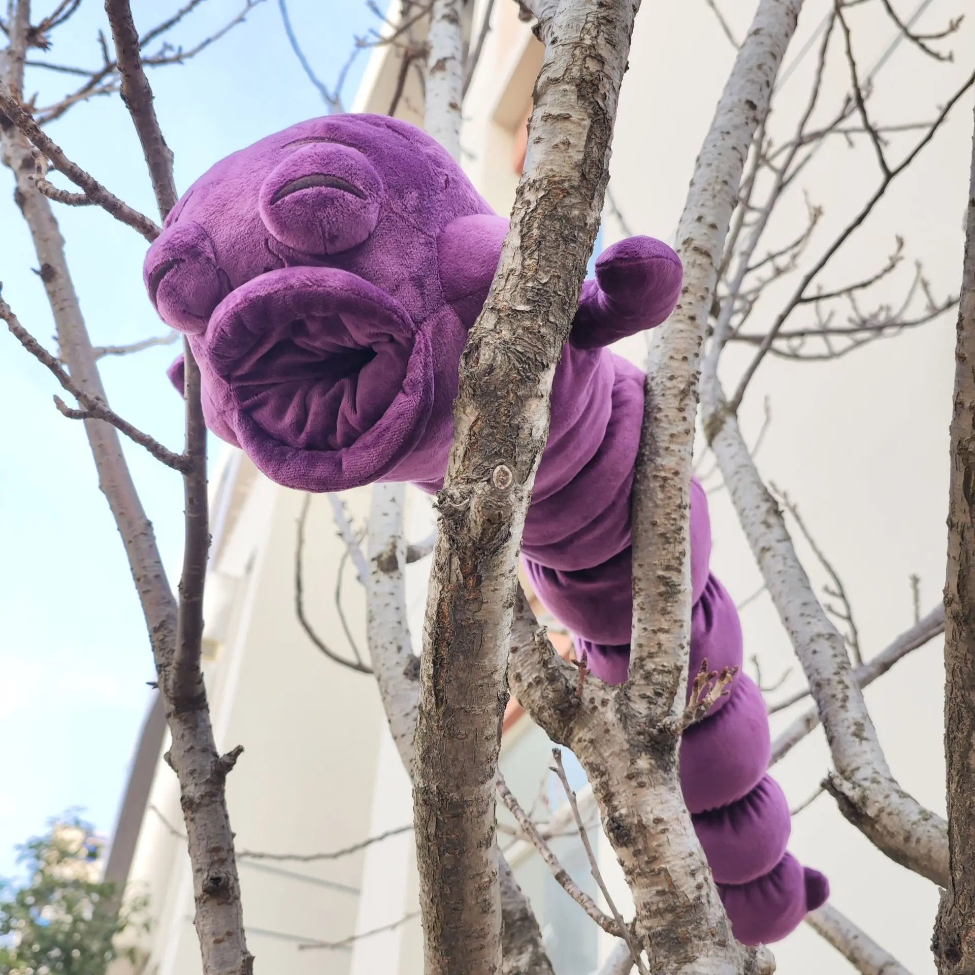 Peluche violette, accrochée à une branche avec patte enroulée, texture duveteuse.